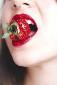 woman with red lipstick biting strawberry